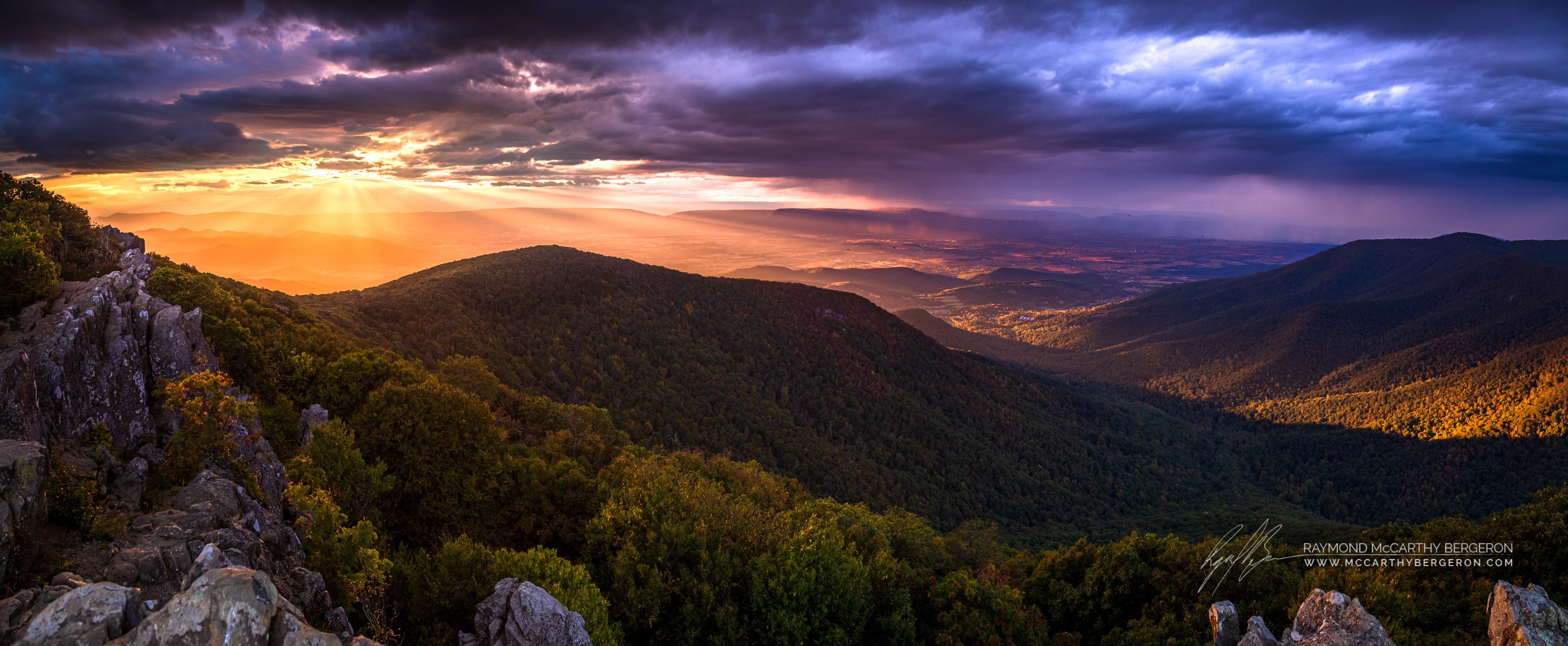 Panoramic view of a mountain landscape with a dramatic sky at sunset.
